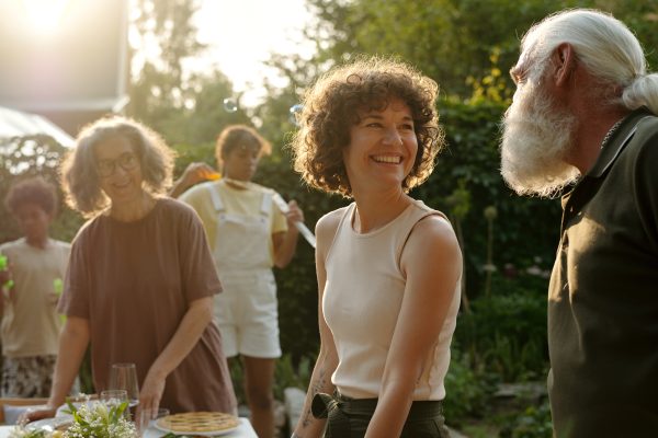 Young cheerful brunette woman looking at her father while serving table for outdoor family together against grandmothern and grandchildren